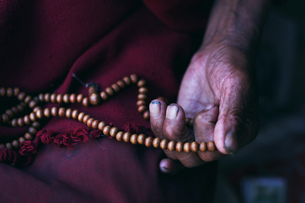 Gros plan sur la main d'un moine en train de prier avec un chapelet en bois, Tibet, Lhatse, extrait du livre 56000 kilomètres